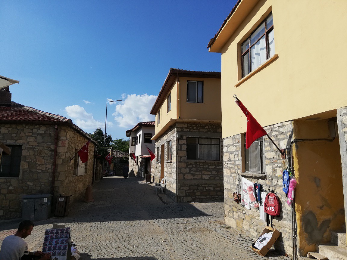 KÖYE VARDIĞIMIZDA ATMOSFER DEĞİŞİYORGideceğimiz köy, adı gibi Taşlı Tepe'nin güney yamaçlarında yer alıyor. İlçeye uzaklığı sadece 7 kilometre ama biz yine de kendisine zor ulaşıyoruz. Sonunda köye varıyoruz. Köyü bulmak zor belki ama içine girdiğimizde bu çabaya değdiğini anlıyoruz.